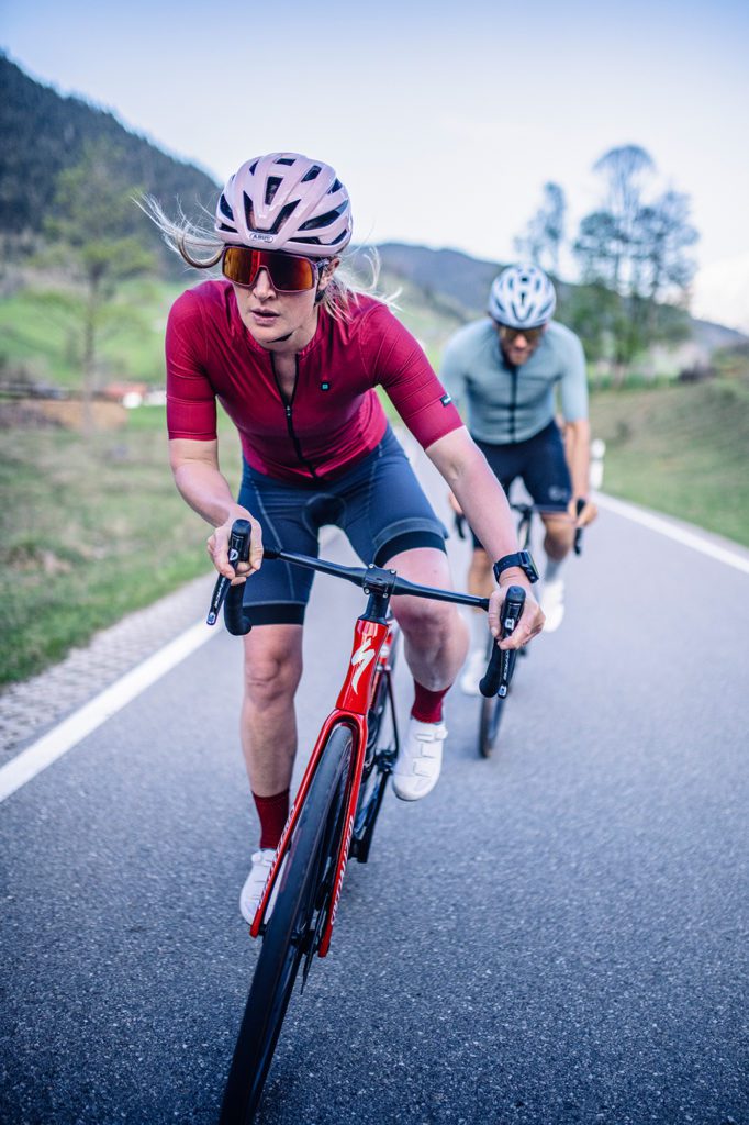 Frau mit rosa Helm auf Rennrad vor Mann