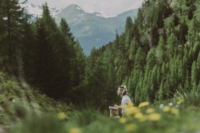Frau sitzt auf einer Bergwiese beim Journaling