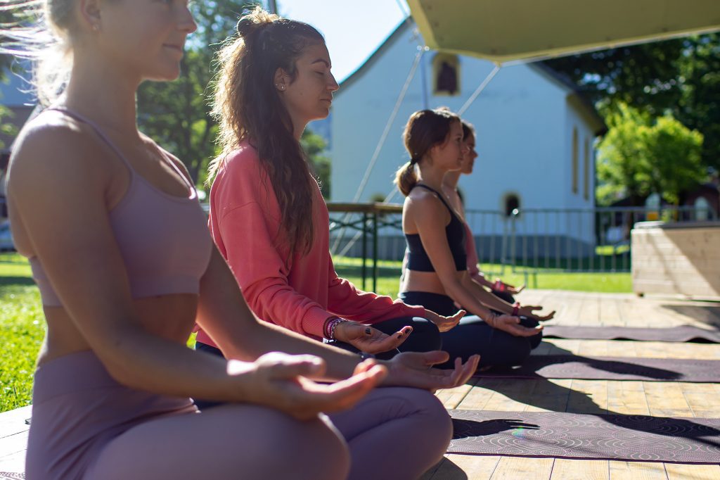 Drei Frauen sitzen im Schneidersitz auf Yogamatte und machen Atemübungen