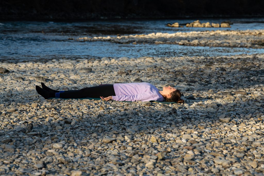 Frau liegt in Savasana auf Yogamatte an Fluss