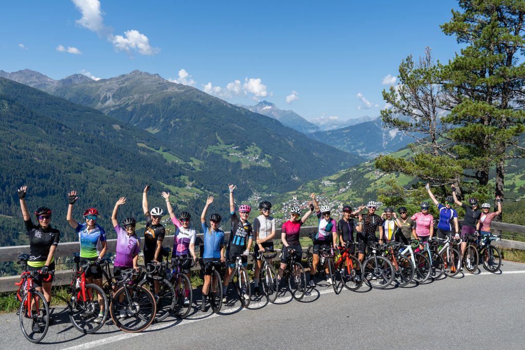 Gruppen von Radfahrerinnen steht auf Straße und wirft die Hände in die Höhe