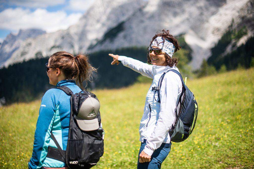 Zwei Frauen stehen vor Berg und eine zeigt in die Ferne