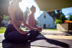 Frauen sitzen auf Yogamatte in Morgensonne beim Meditieren